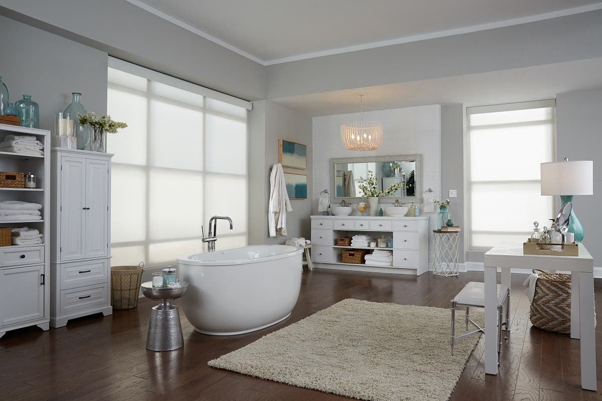 Spacious white bathroom with soaking tub in the middle and fully closed sheer roller shades